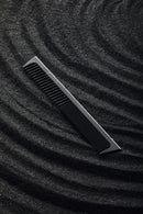 A professional hair comb from Joseph Orozco, designed for styling, rests diagonally on a textured, shimmering black surface that suggests the sleekness and elegance of the styling tools and products by this pro hair brand.