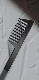 An elegantly designed Joseph Orozco professional hair comb for detangling is showcased on a textured white surface with streaks of hair product. The comb's matte black finish provides a stark contrast against the white, highlighting its role as a sophisticated styling tool in the world of professional hair care.